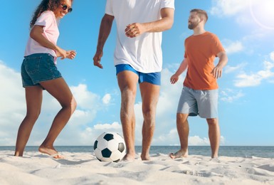 Happy friends playing football on beach during sunny day, low angle view