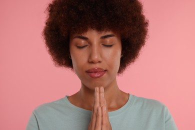 Woman with clasped hands praying to God on pink background