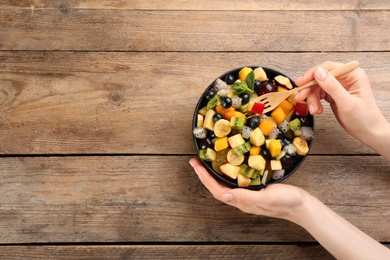 Woman with delicious exotic fruit salad at wooden table, top view. Space for text