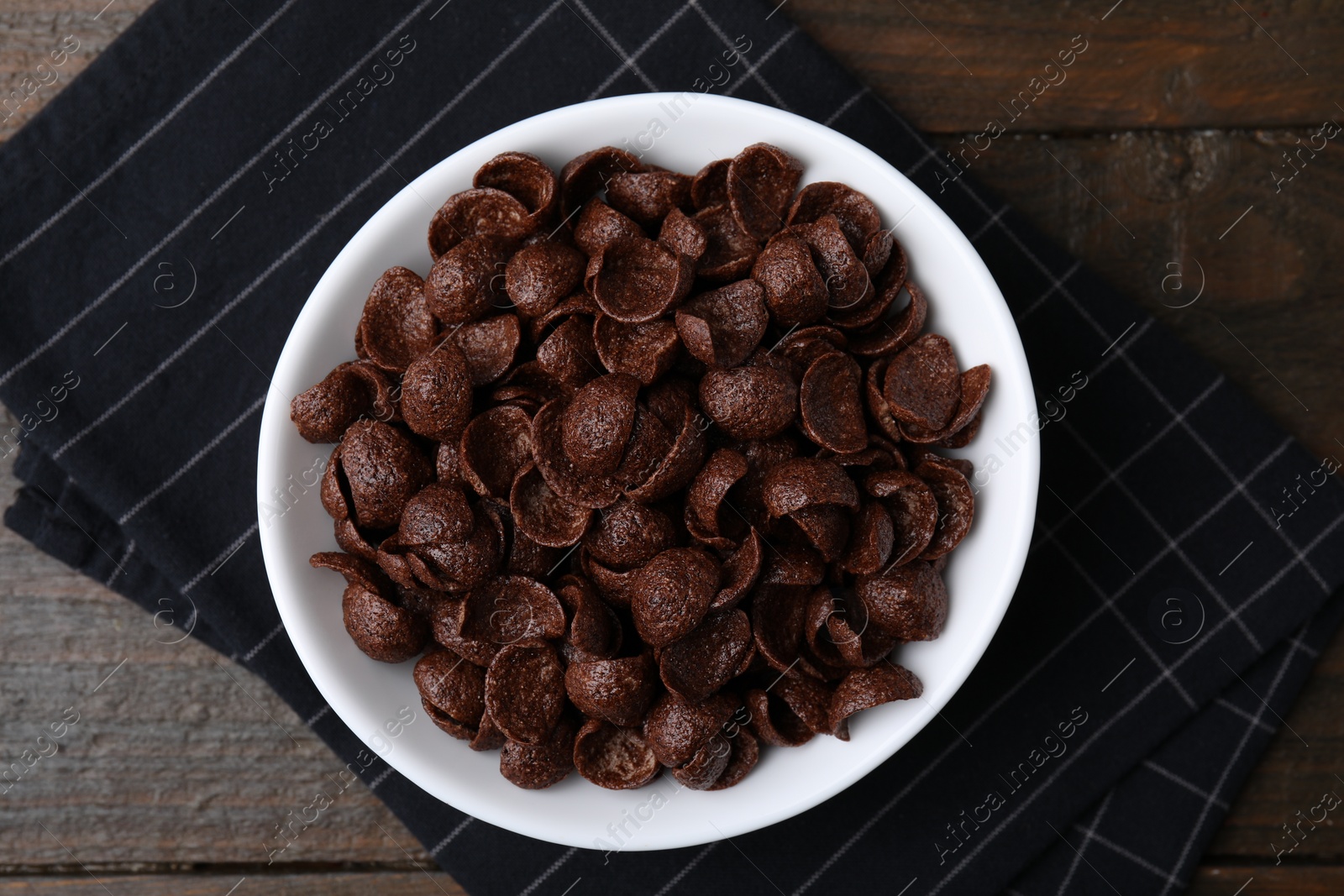 Photo of Chocolate corn flakes in bowl on wooden table, top view. Breakfast cereal