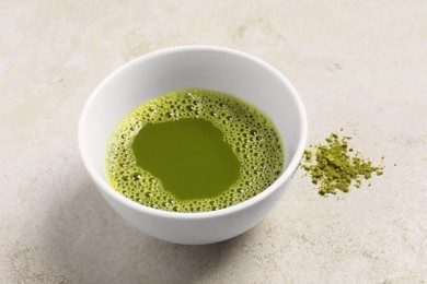 Photo of Cup of matcha tea on light gray textured table, closeup