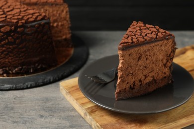 Photo of Piece of delicious chocolate truffle cake and fork on grey textured table, closeup