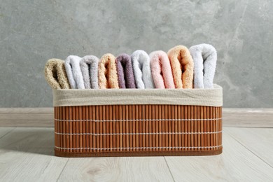 Photo of Laundry basket with clean terry towels on floor near grey wall