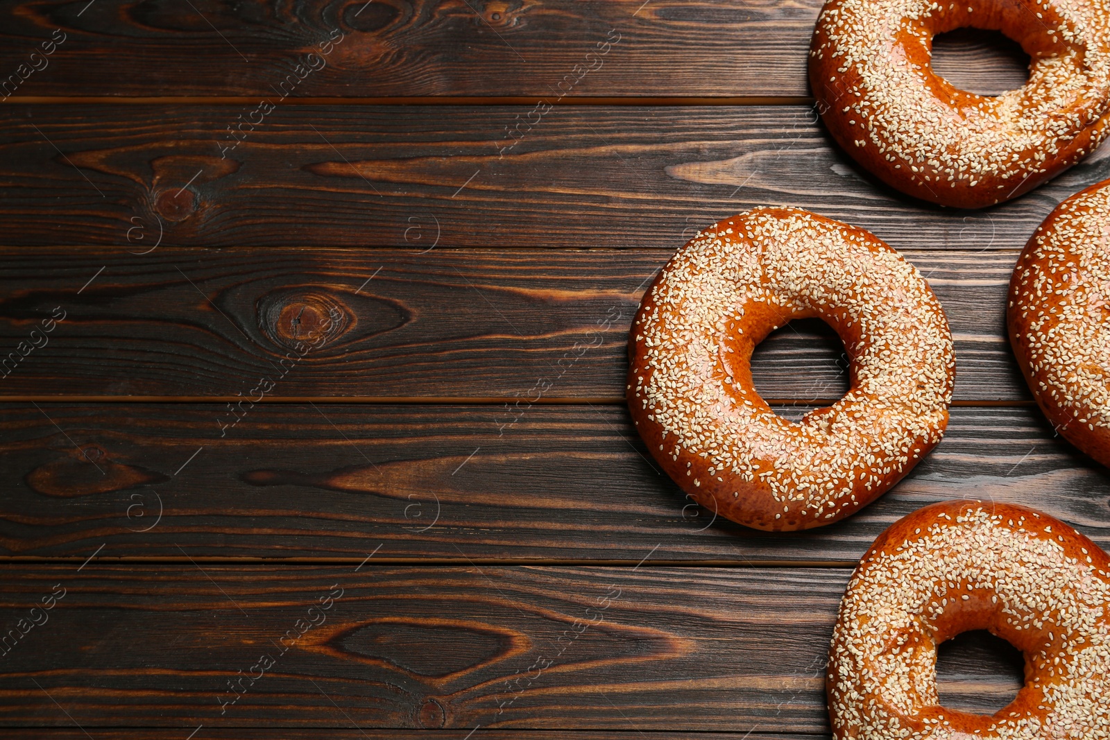 Photo of Delicious fresh bagels with sesame seeds on wooden table, flat lay. Space for text