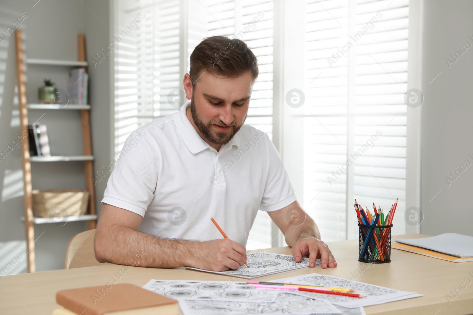 Photo of Young man coloring antistress picture at table indoors