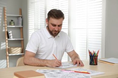 Young man coloring antistress picture at table indoors