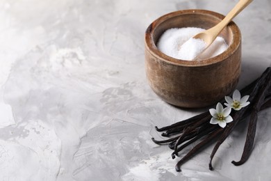 Vanilla pods, flowers and bowl with sugar on light textured table, closeup. Space for text