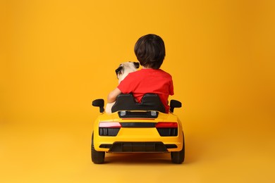 Little boy with his dog in toy car on yellow background, back view