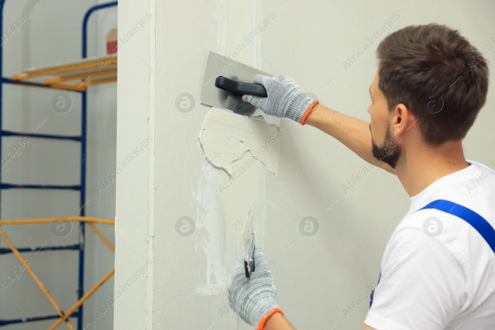 Photo of Professional worker plastering wall with putty knives indoors