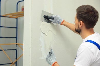 Professional worker plastering wall with putty knives indoors