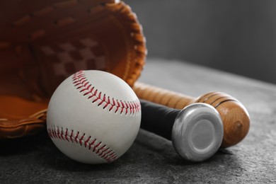 Photo of Baseball bats, glove and ball on grey table, closeup