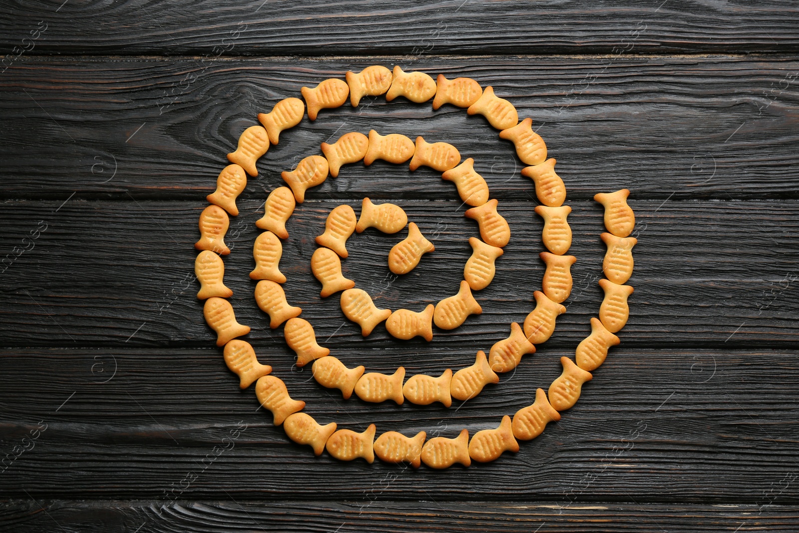 Photo of Delicious goldfish crackers on black wooden table, flat lay