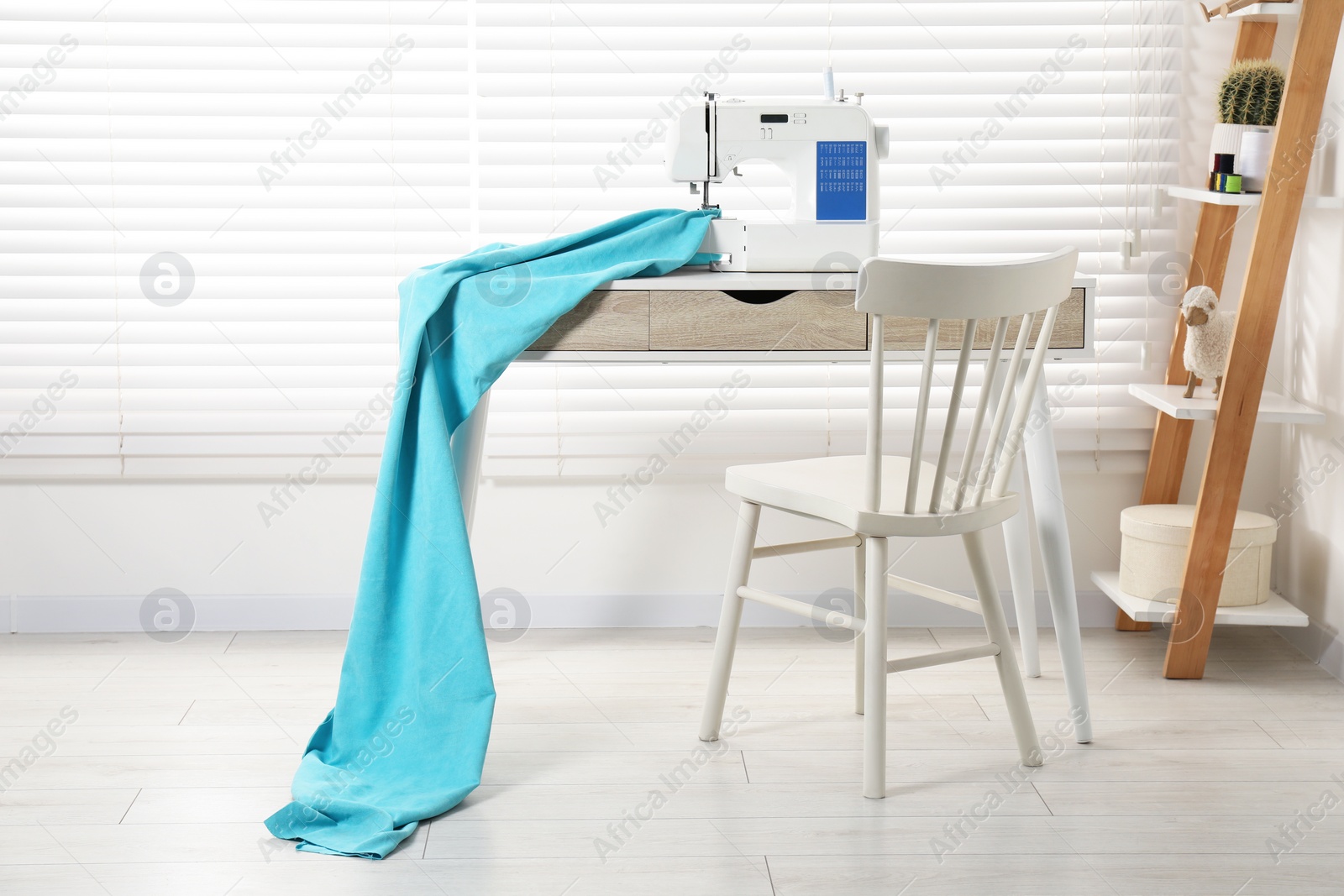 Photo of White sewing machine and fabric on wooden desk near chair indoors