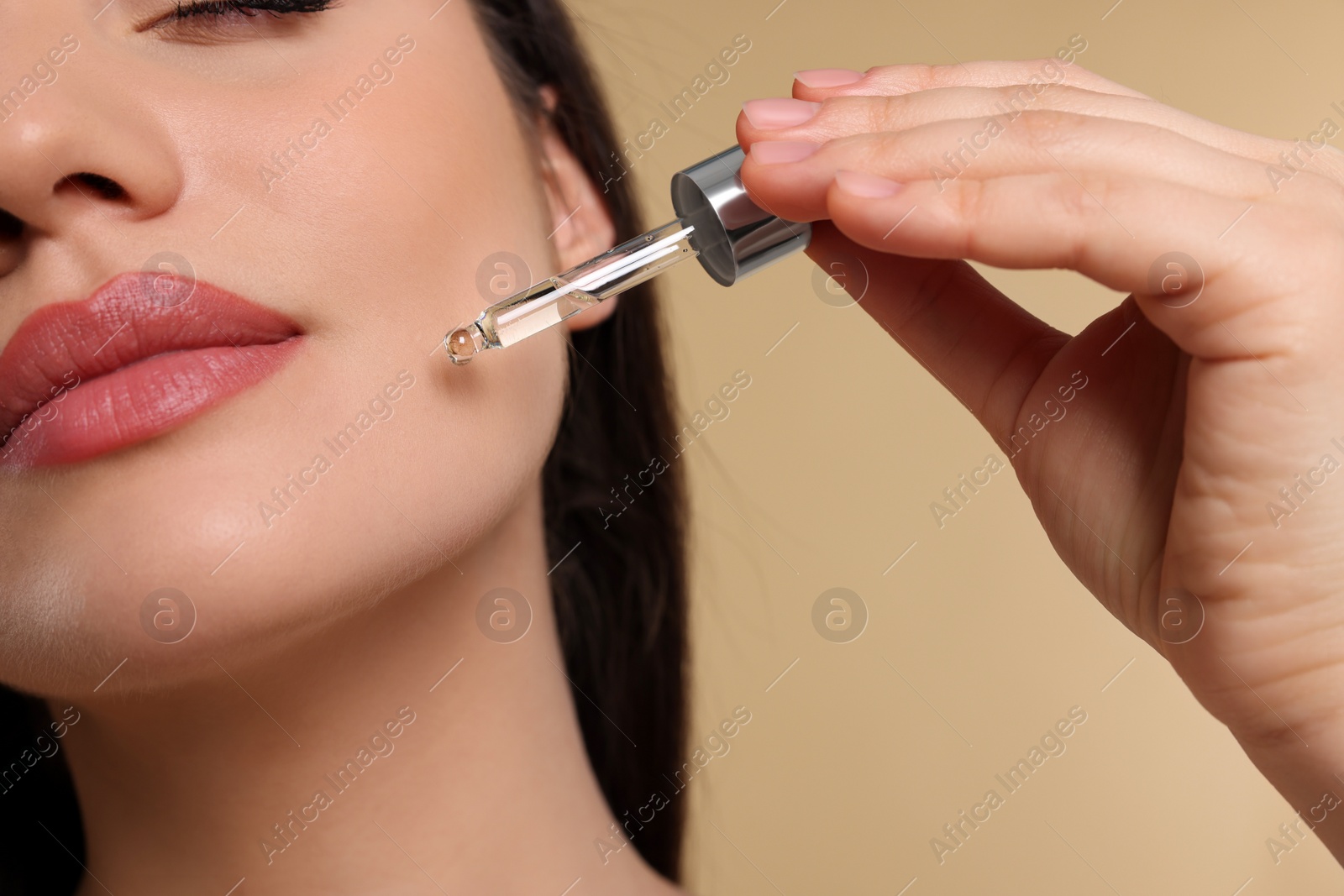 Photo of Young woman applying essential oil onto face on beige background, closeup