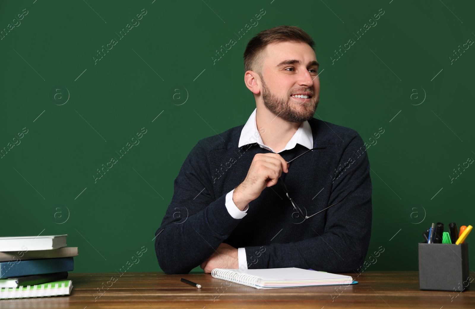 Photo of Portrait of young teacher at table against green background. Space for text