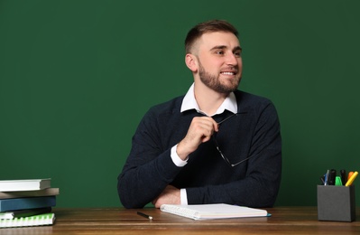 Portrait of young teacher at table against green background. Space for text