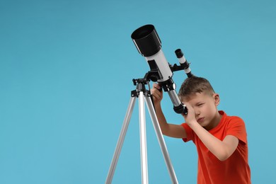 Little boy looking at stars through telescope on light blue background, space for text
