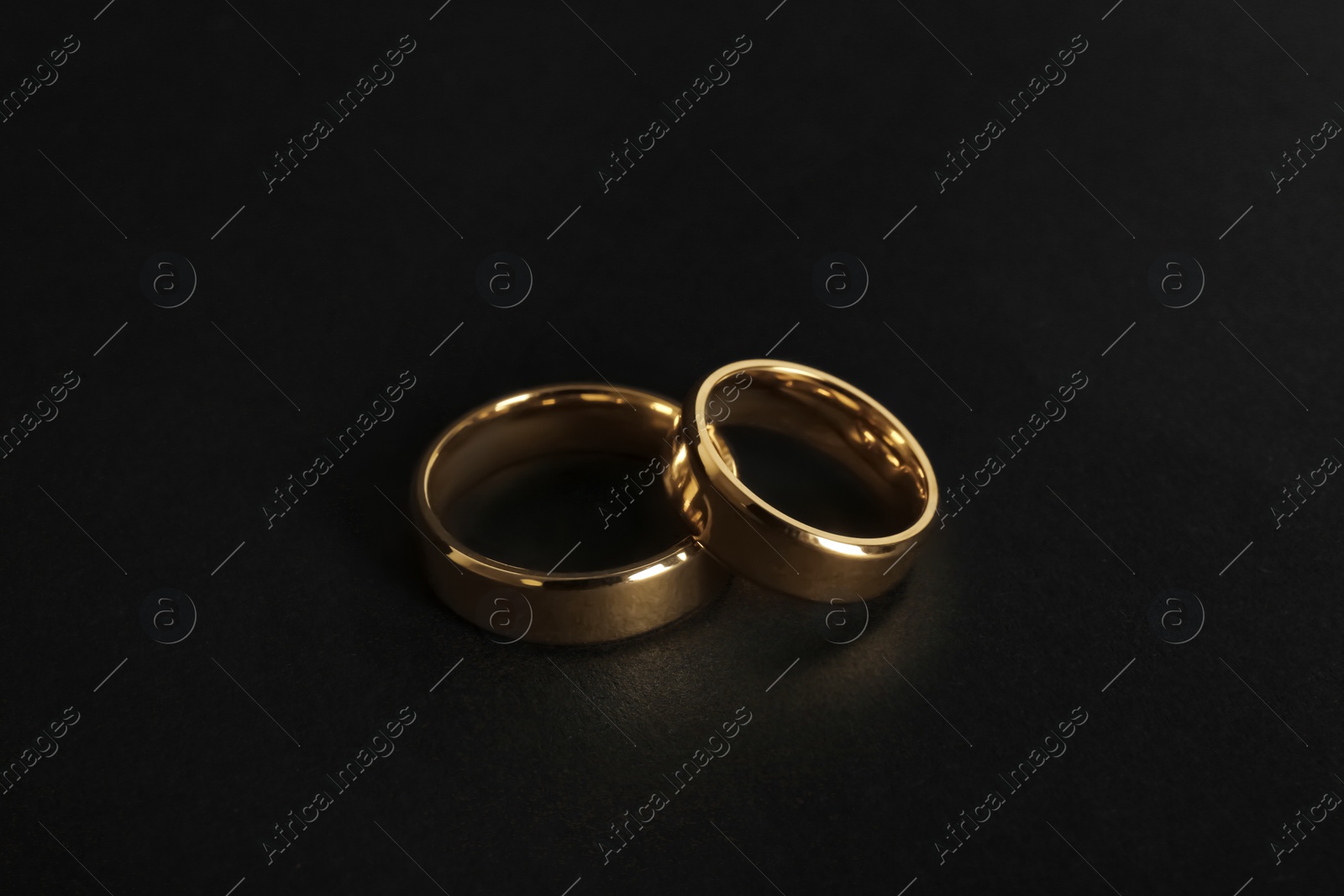 Photo of Beautiful gold wedding rings on black background