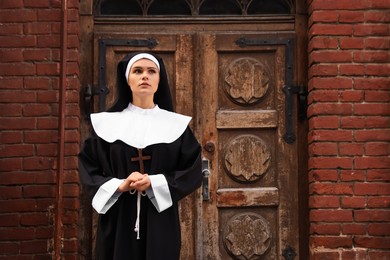 Young nun with Christian cross near old building outdoors