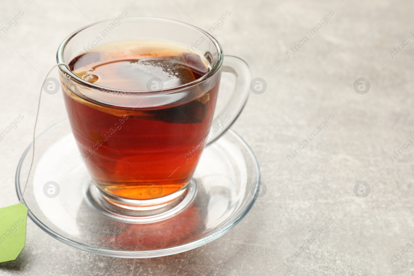 Photo of Brewing tea. Glass cup with tea bag on light table, closeup. Space for text