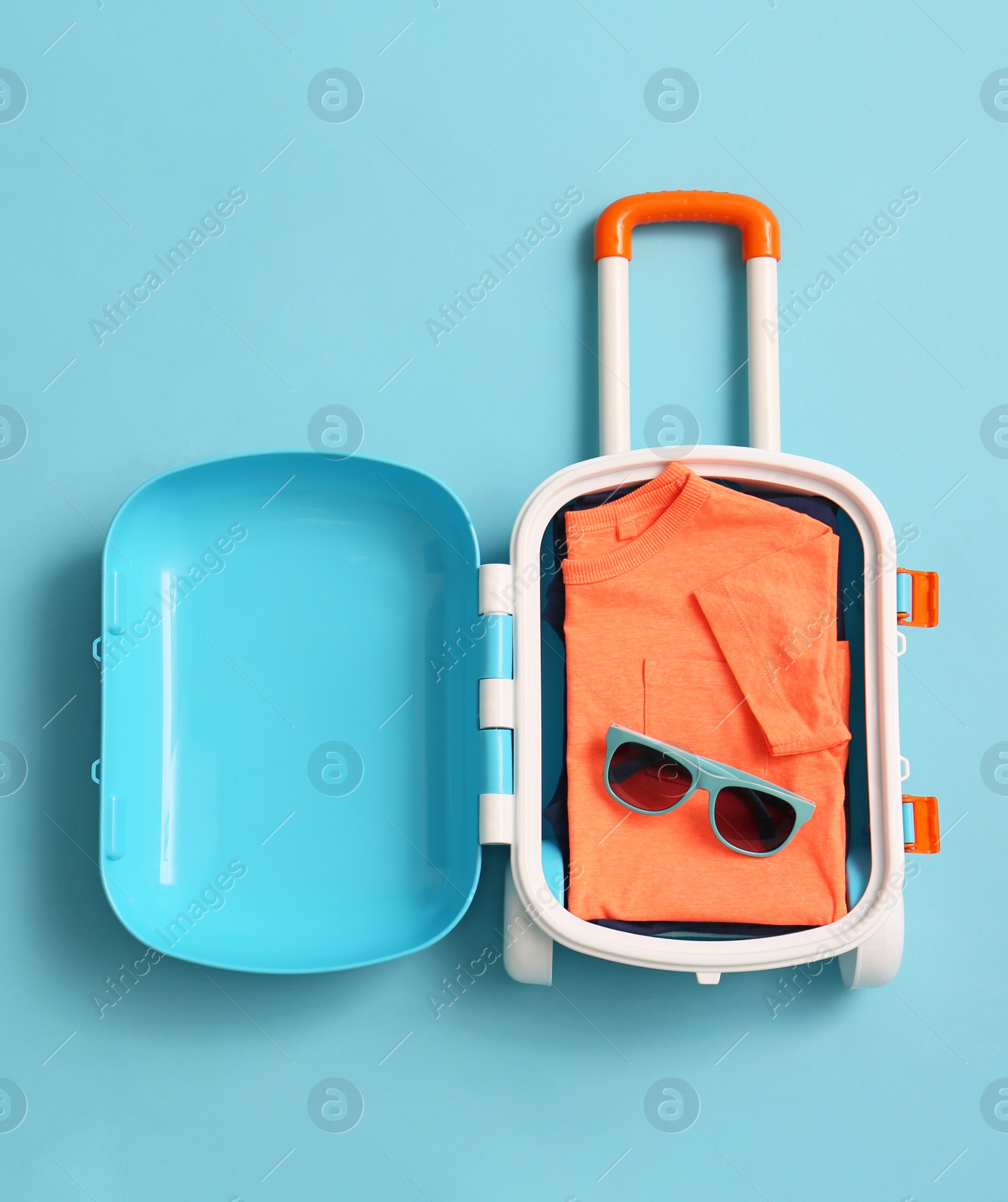 Photo of Child suitcase with clothes and sunglasses on blue background, top view. Space for text