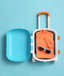 Photo of Child suitcase with clothes and sunglasses on blue background, top view. Space for text