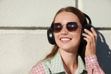 Photo of Smiling woman in headphones listening to music near white wall outdoors. Space for text