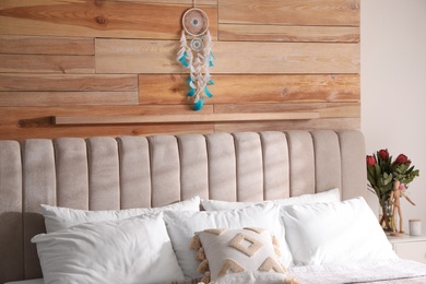 Beautiful dream catcher hanging above bed in stylish room interior