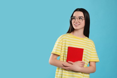 Photo of Happy teenage girl in glasses with textbook on light blue background. Space for text