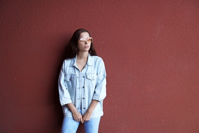 Young hipster woman in stylish jeans and jacket posing near color wall