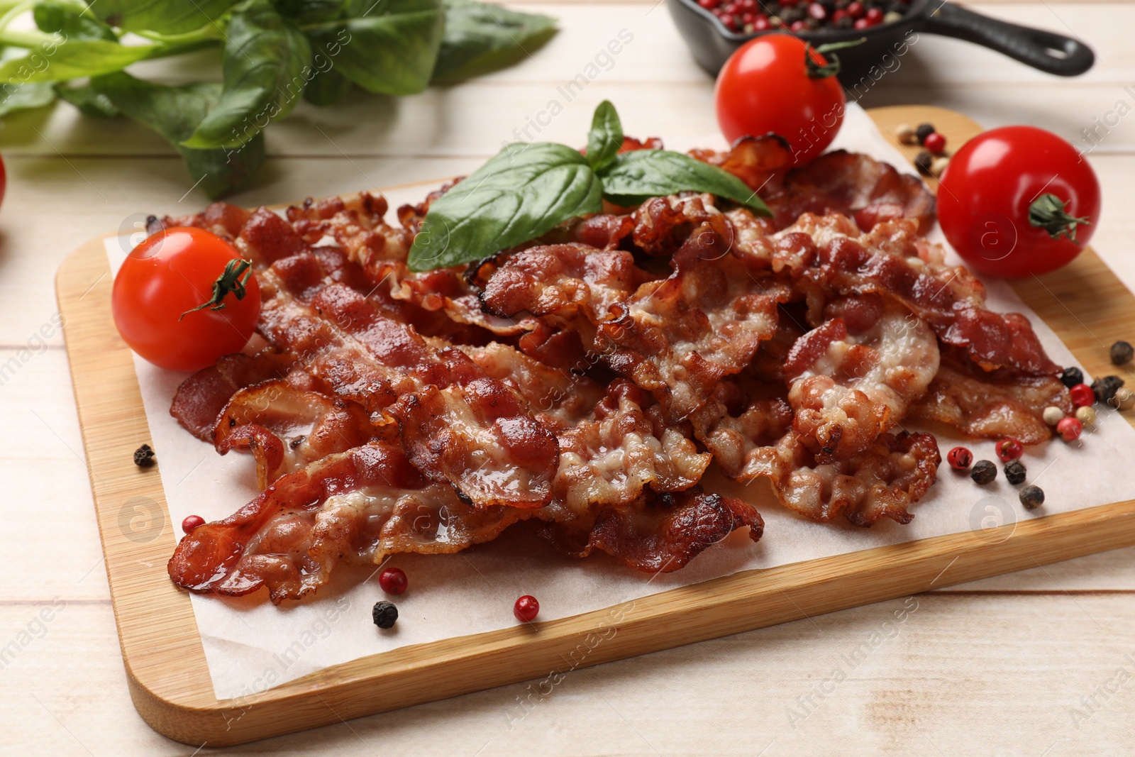 Photo of Slices of tasty fried bacon with different spices and tomatoes on wooden table