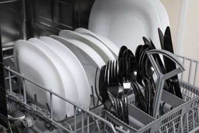 Open modern dishwasher with clean tableware, closeup