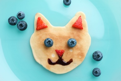 Photo of Tasty pancake served with berries on blue plate, flat lay. Creative idea for kids breakfast