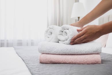 Photo of Woman putting soft clean towels on bed indoors, closeup. Space for text