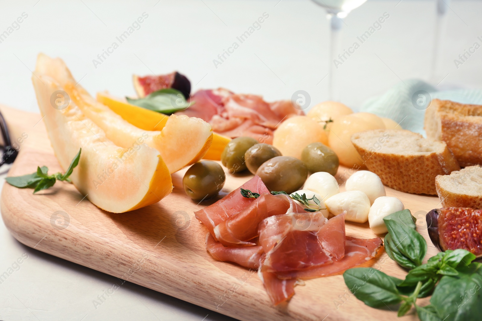 Photo of Cutting board with melon and prosciutto appetizer on light table