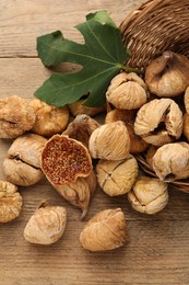 Overturned wicker basket, dried figs and green leaf on wooden table, flat lay