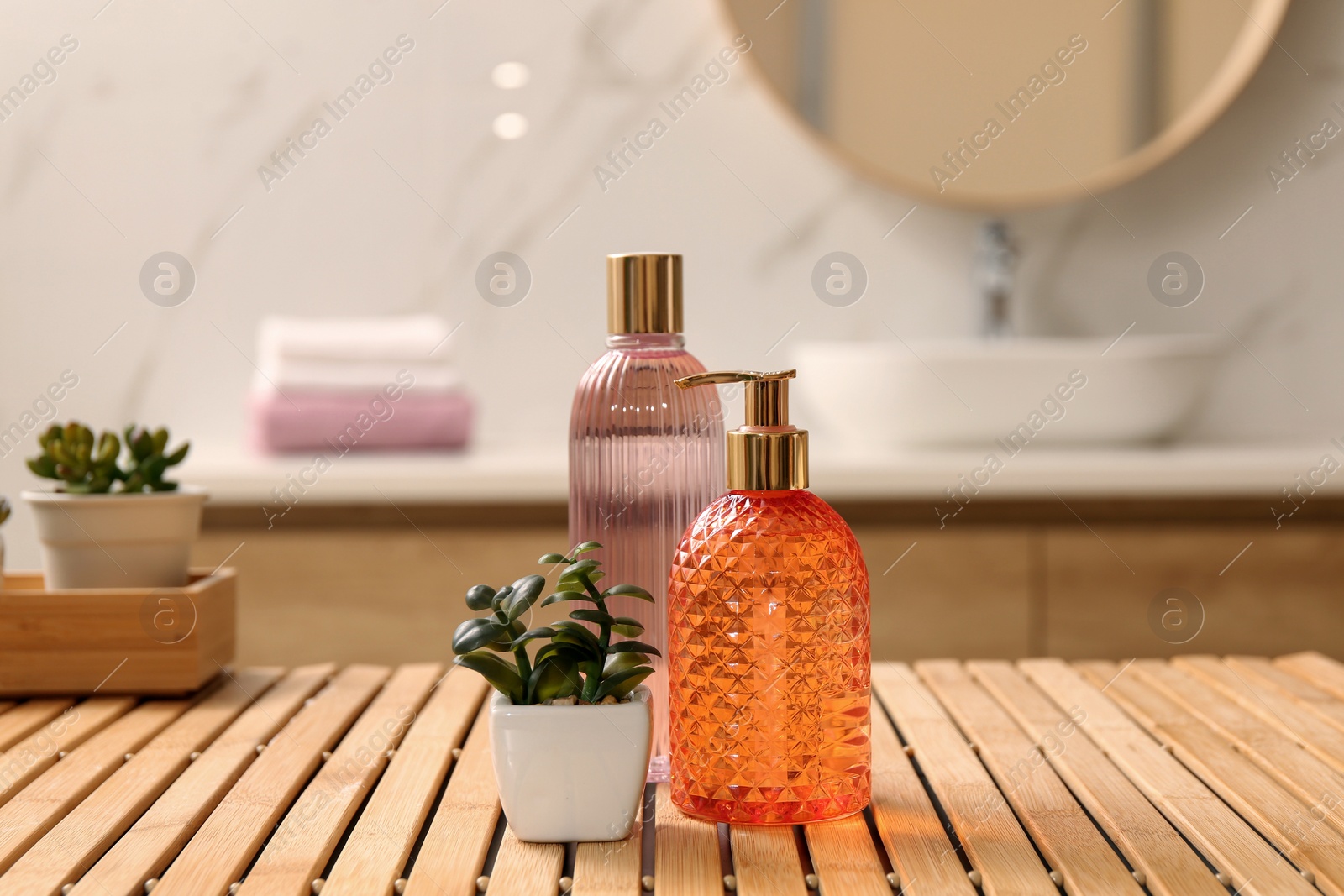 Photo of Glass dispenser with liquid soap, bottle of gel and plants on wooden table in bathroom