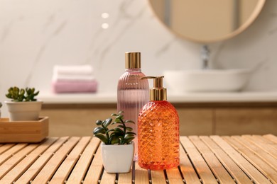 Photo of Glass dispenser with liquid soap, bottle of gel and plants on wooden table in bathroom