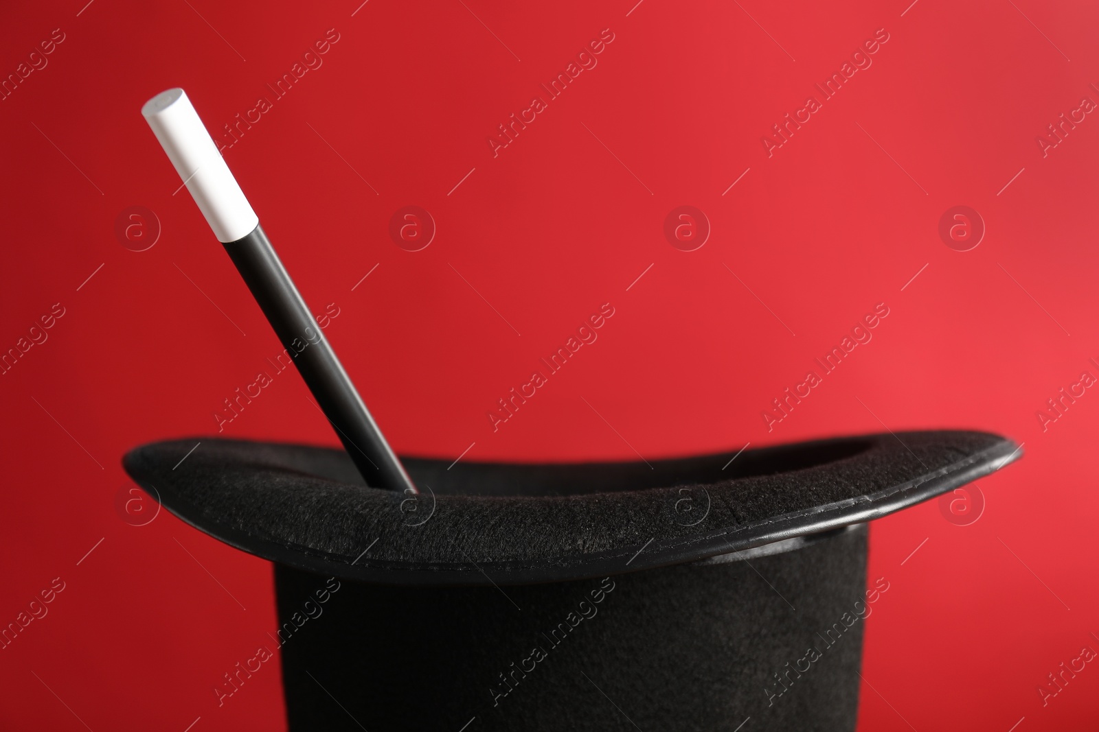 Photo of Black magician's hat and wand on red background, closeup