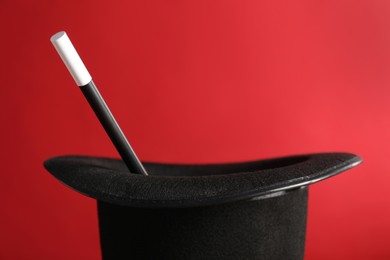 Photo of Black magician's hat and wand on red background, closeup