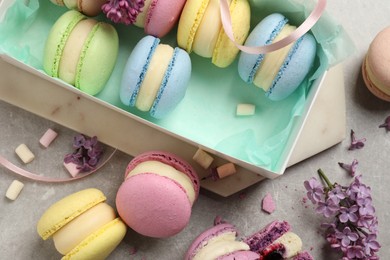 Photo of Delicious colorful macarons, marshmallows and lilac flowers on grey table, flat lay