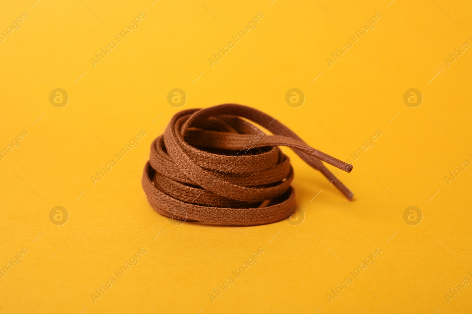 Photo of Brown shoe lace on yellow background. Stylish accessory