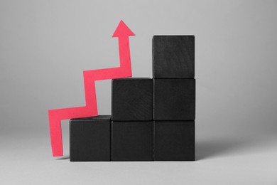 Photo of Economic profit. Stacked black wooden cubes and arrow on light grey background