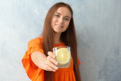 Photo of Young woman holding glass of lemon water on color background