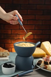 Woman dipping piece of potato into fondue pot with melted cheese at table with snacks, closeup