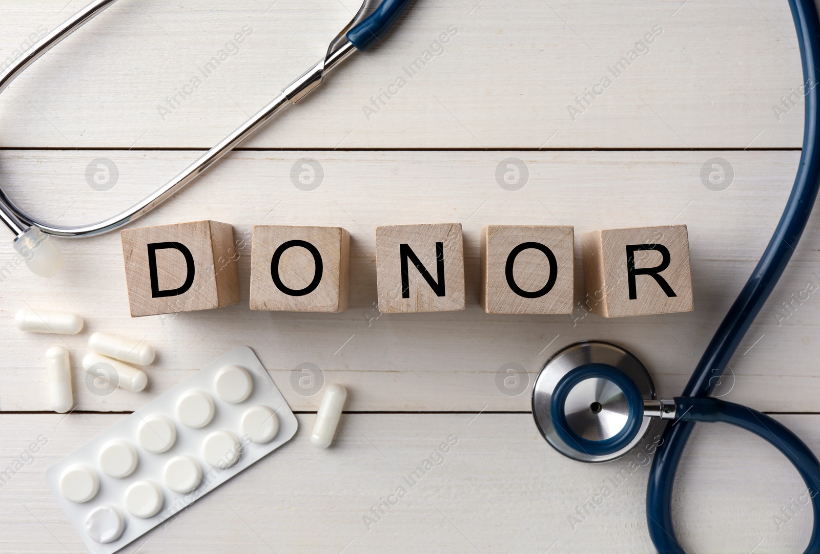 Photo of Word Donor made of cubes, stethoscope and pills on white wooden table, flat lay