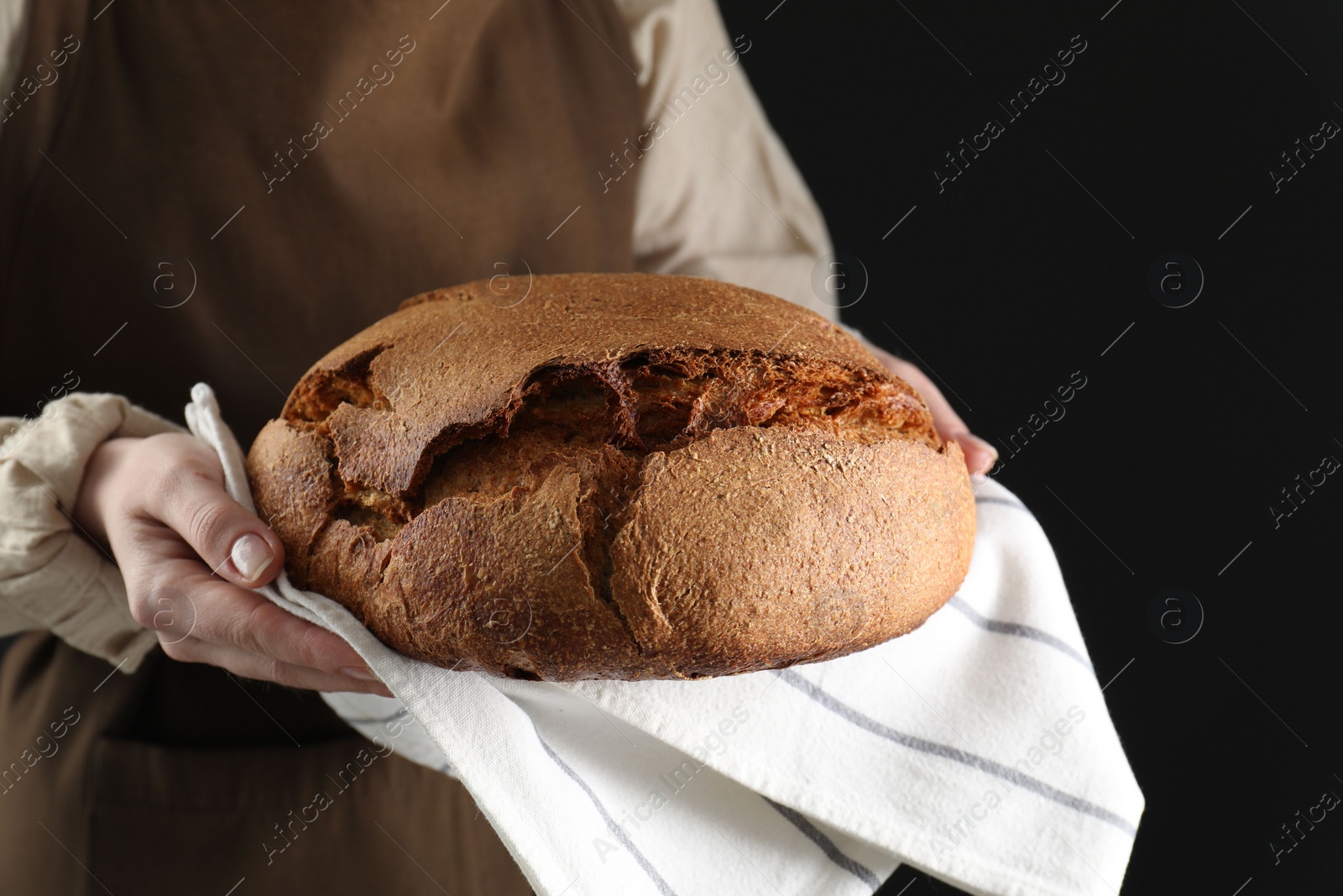 Photo of Woman holding freshly baked bread on black background, closeup