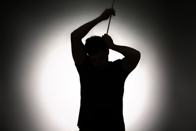 Silhouette of man with rope noose on neck against light background