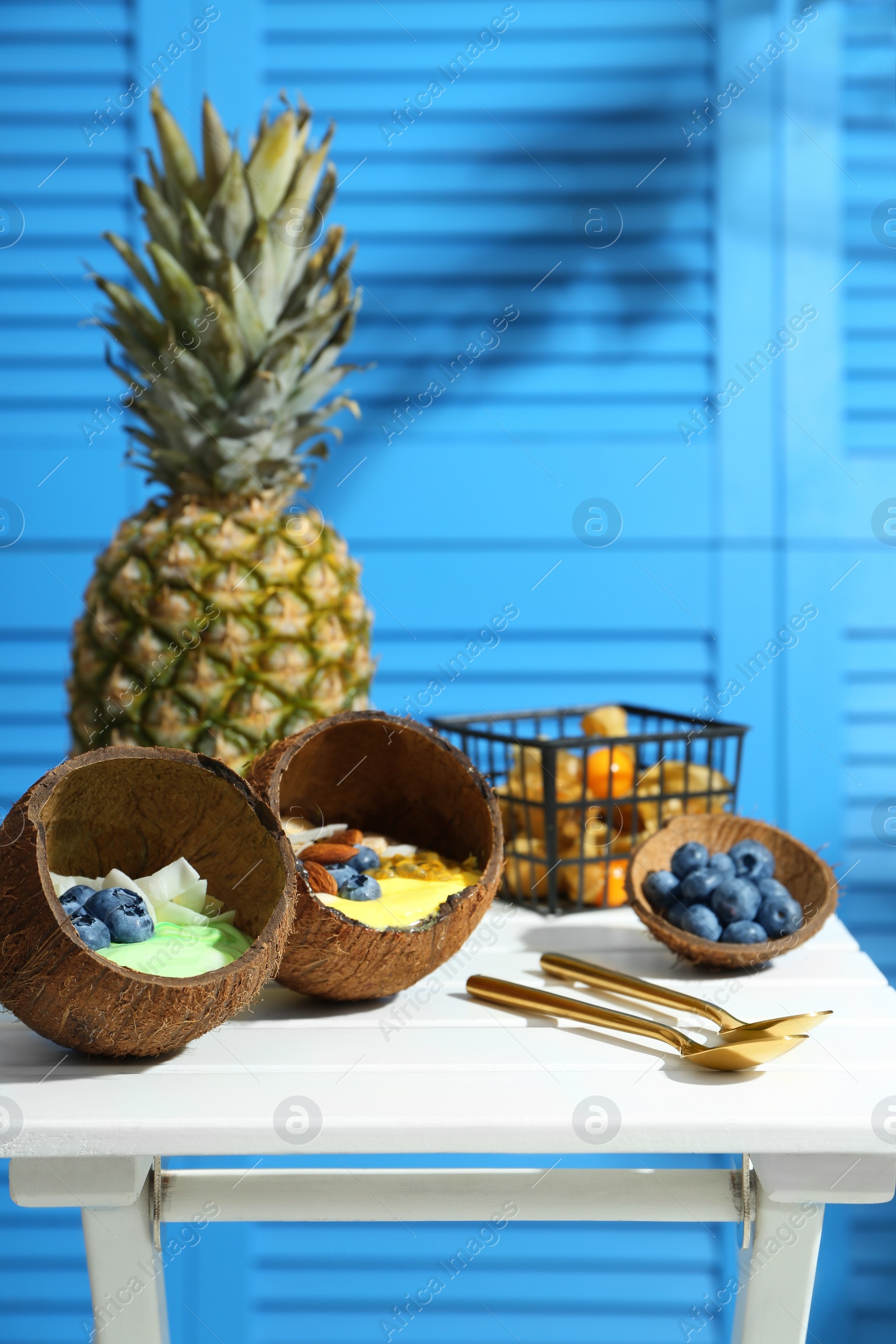 Photo of Tasty smoothie bowl served in coconut shells on white wooden table