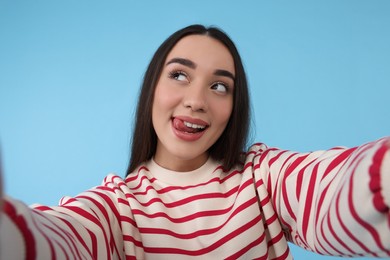 Young woman taking selfie on light blue background